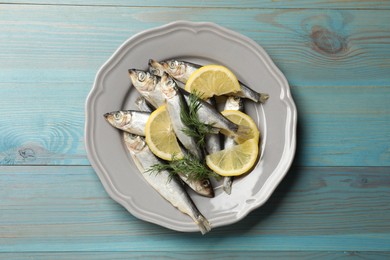 Photo of Fresh raw sprats, dill and cut lemon on light blue wooden table, top view