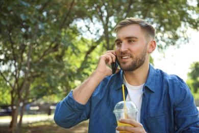 Photo of Young man with refreshing drink talking on smartphone in park