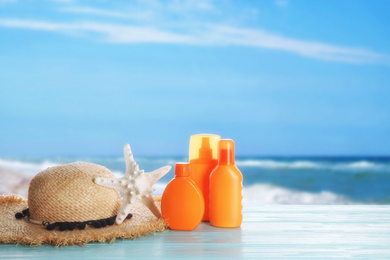 Image of Set of sun protection products and stylish hat on blue wooden table near sea. Space for text