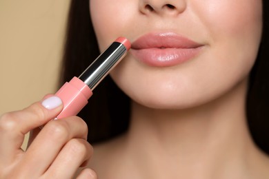 Photo of Young woman applying nude lipstick on beige background, closeup