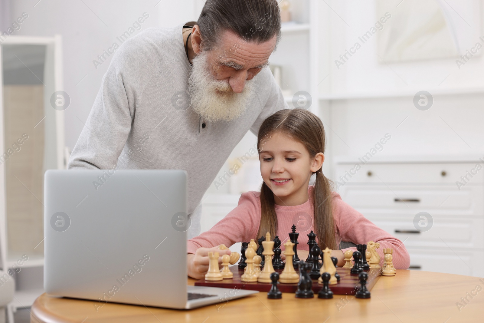 Photo of Grandfather teaching his granddaughter to play chess following online lesson at home