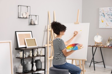 Photo of Young woman painting on easel with canvas in studio