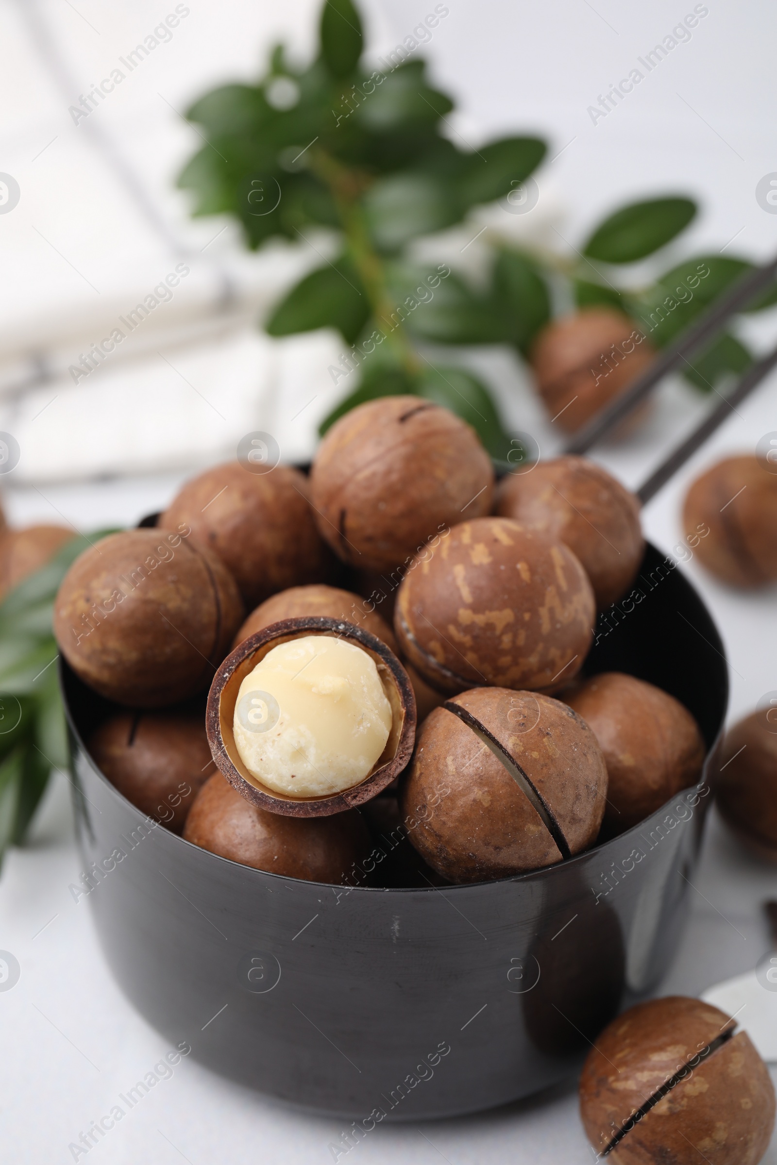 Photo of Tasty organic Macadamia nuts in small saucepan on white table, closeup