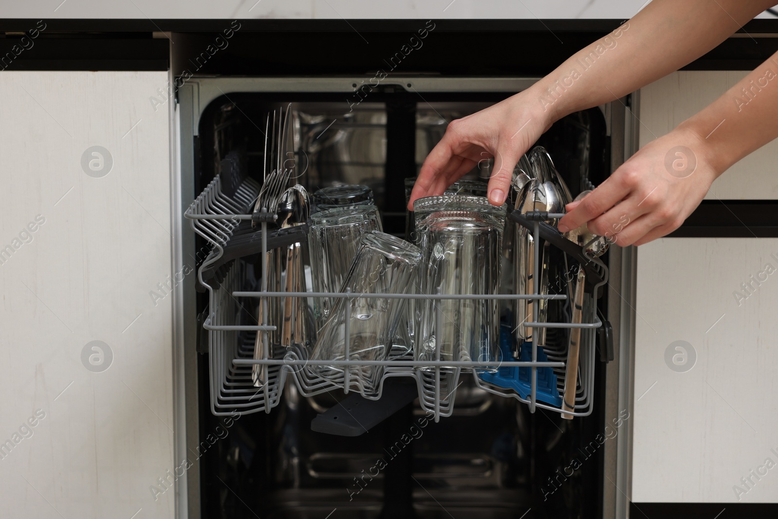 Photo of Woman loading dishwasher with glass and cutlery indoors, closeup