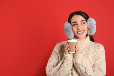 Photo of Beautiful young woman in earmuffs with cup of drink on red background. Space for text