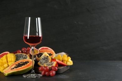 Photo of Delicious exotic fruits and glass of wine on black table, space for text