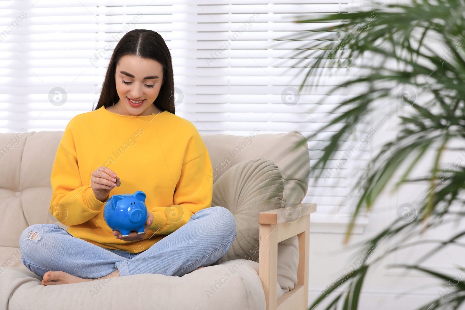 Photo of Young woman putting coin into piggy bank at home