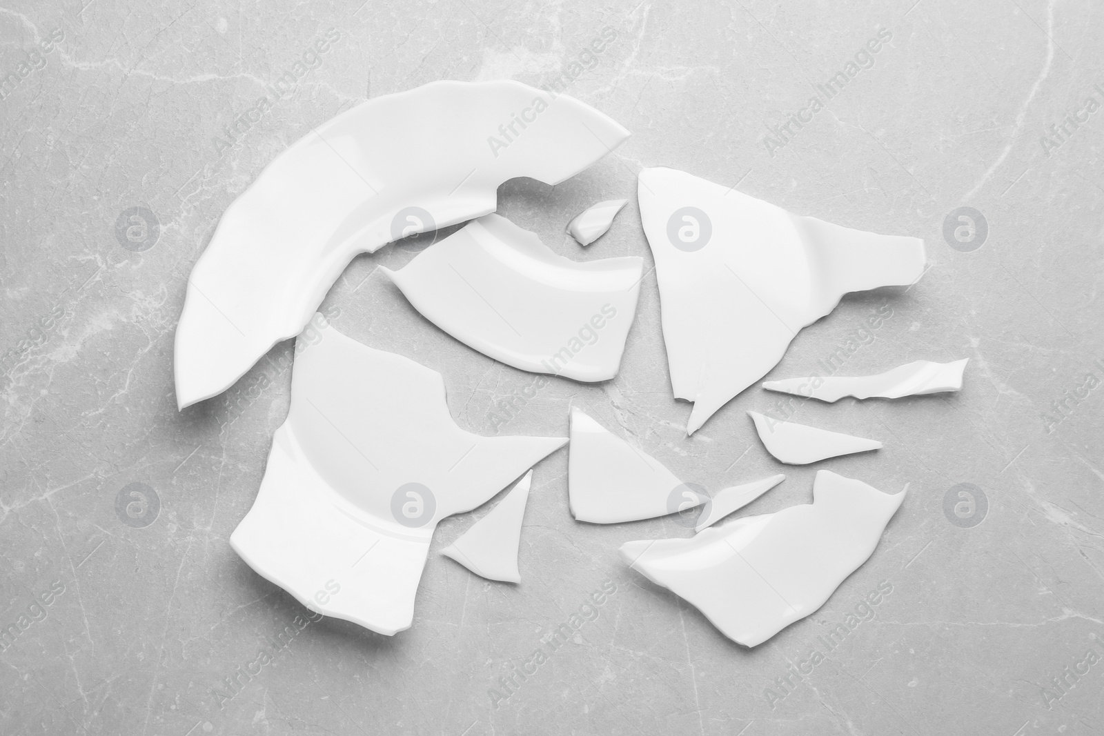 Photo of Pieces of broken ceramic plate on light grey table, flat lay