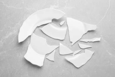 Photo of Pieces of broken ceramic plate on light grey table, flat lay