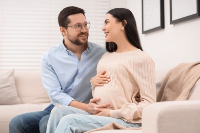 Photo of Happy pregnant woman spending time with her husband on sofa at home