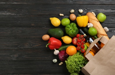 Photo of Flat lay composition with overturned paper bag and groceries on black wooden background. Space for text