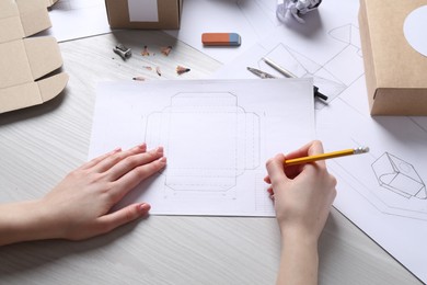 Photo of Woman creating packaging design at light wooden table, closeup