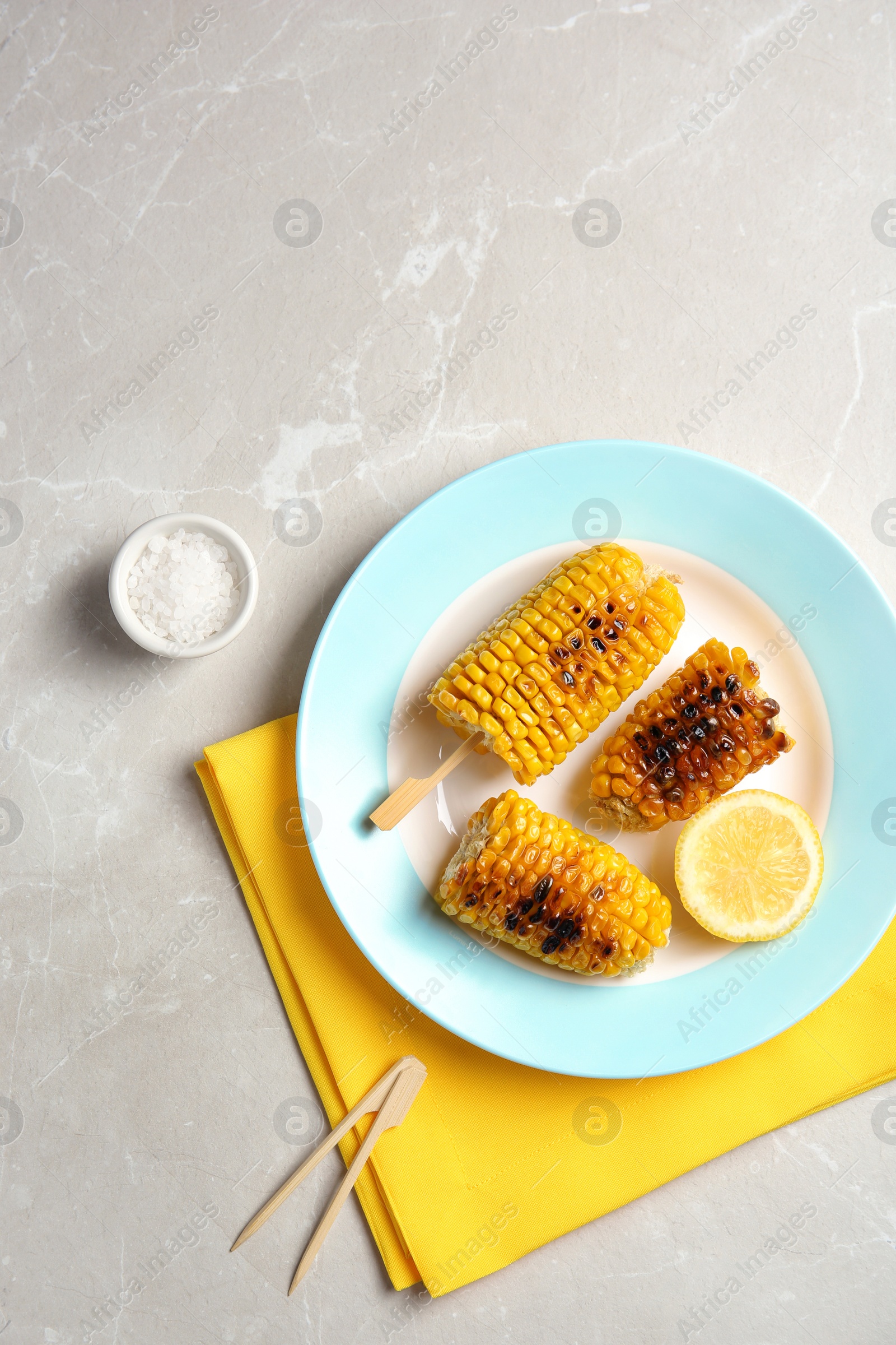 Photo of Plate with delicious grilled corn cobs on light table, top view. Space for text