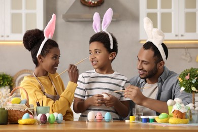 Happy African American family having fun while painting Easter eggs at table in kitchen