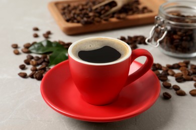 Cup of aromatic hot coffee and beans on light grey table