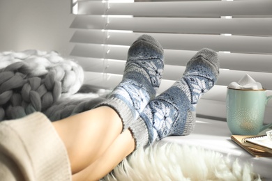 Woman with cocoa wearing knitted socks at home, closeup. Warm clothes