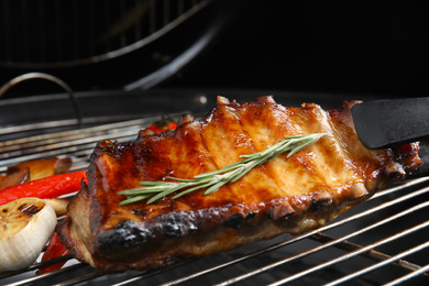 Photo of Delicious ribs with rosemary and vegetables on barbecue grill