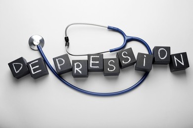 Photo of Word Depression made of black wooden cubes and stethoscope on white background, flat lay