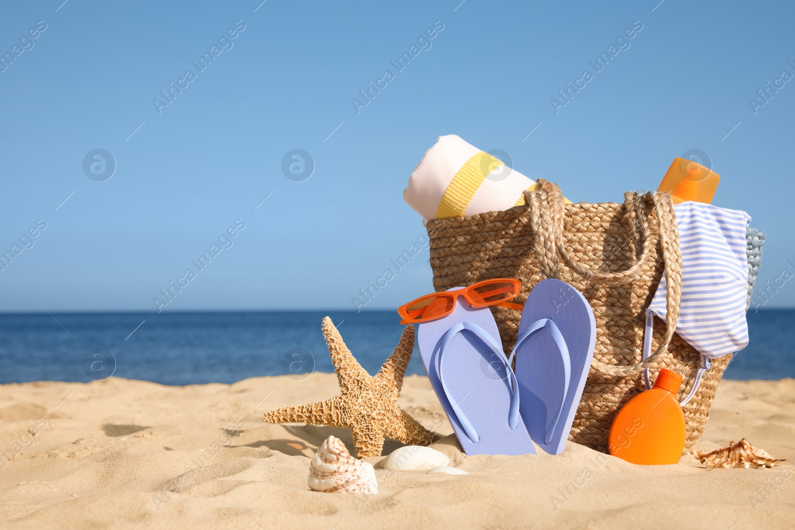 Photo of Bag and beach accessories on sand near sea. Space for text