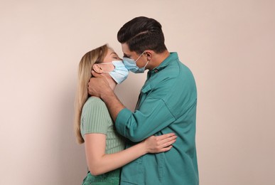 Photo of Couple in medical masks trying to kiss on beige background