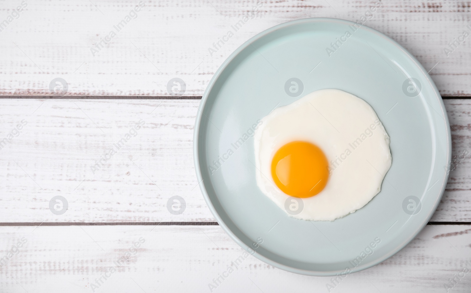 Photo of Tasty fried egg in plate on white wooden table, top view. Space for text