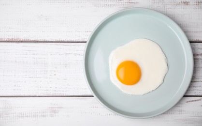 Tasty fried egg in plate on white wooden table, top view. Space for text