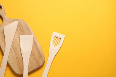 Photo of Different wooden spatulas and board on orange background, flat lay. Space for text