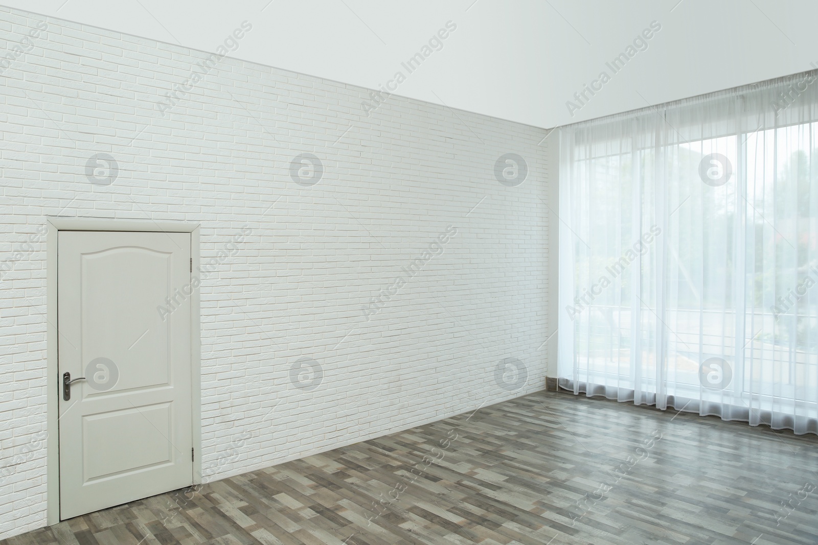 Photo of Empty room with brick wall, large window and white door