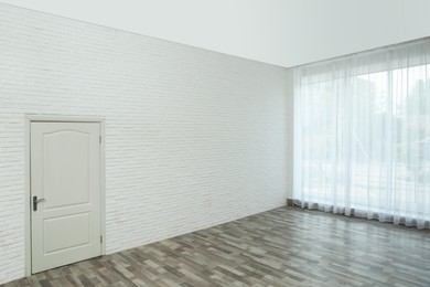 Photo of Empty room with brick wall, large window and white door