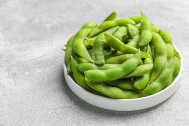 Photo of Plate with green edamame beans in pods on light grey table. Space for text