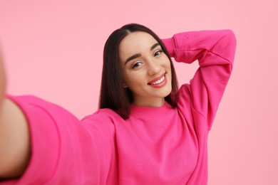 Photo of Smiling young woman taking selfie on pink background