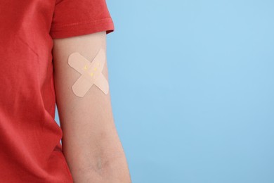 Woman with sticking plaster on her arm against light blue background, closeup. Space for text