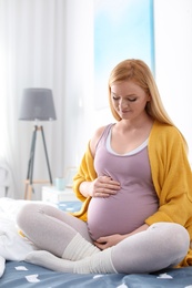 Beautiful pregnant woman sitting on bed in light room