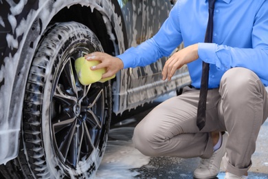 Photo of Businessman cleaning auto with sponge at self-service car wash, closeup