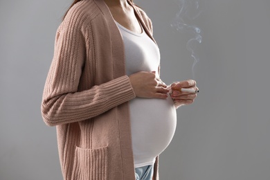 Photo of Young pregnant woman smoking cigarette on grey background, closeup