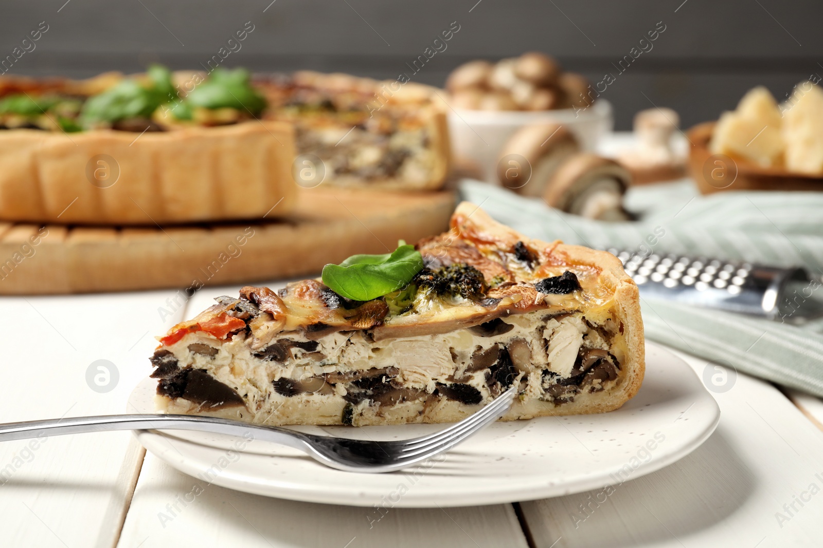 Photo of Piece of delicious quiche with mushrooms and basil served on white wooden table