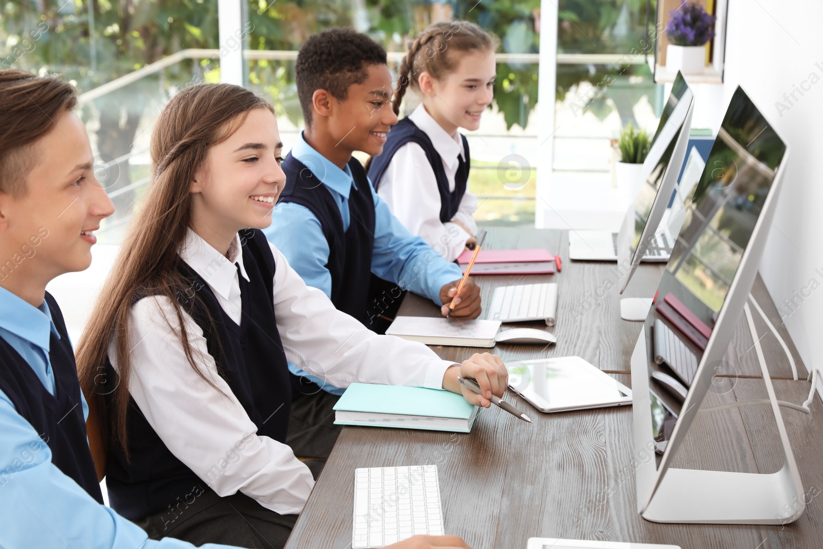 Photo of Teenage students in stylish school uniform at desks with computers