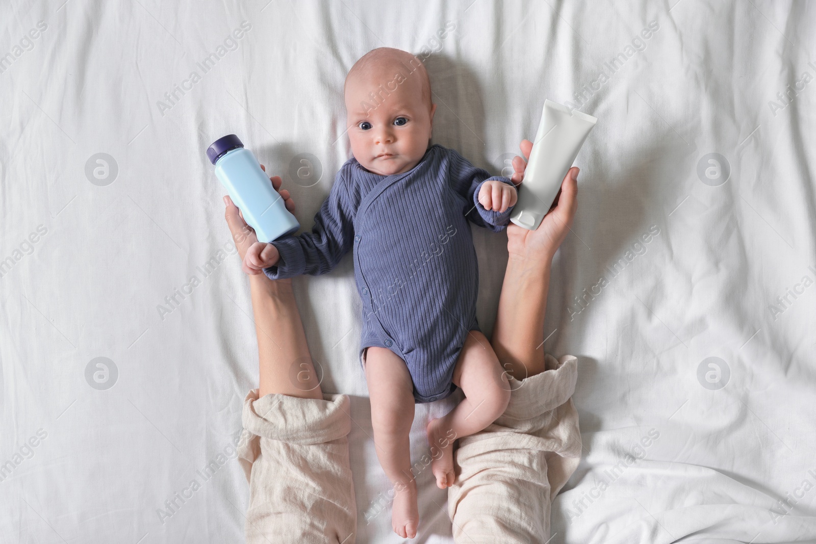 Photo of Mother holding body cream and dusting powder near cute little baby on bed, top view