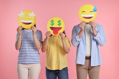 People covering faces with emoticons on pink background