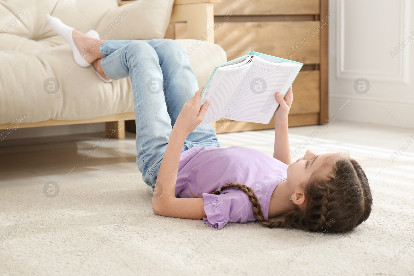 Photo of Cute little girl reading book on floor at home