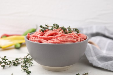 Photo of Fresh raw ground meat and thyme in bowl on white table, closeup