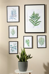 Photo of Beautiful paintings of tropical leaves on beige wall in room