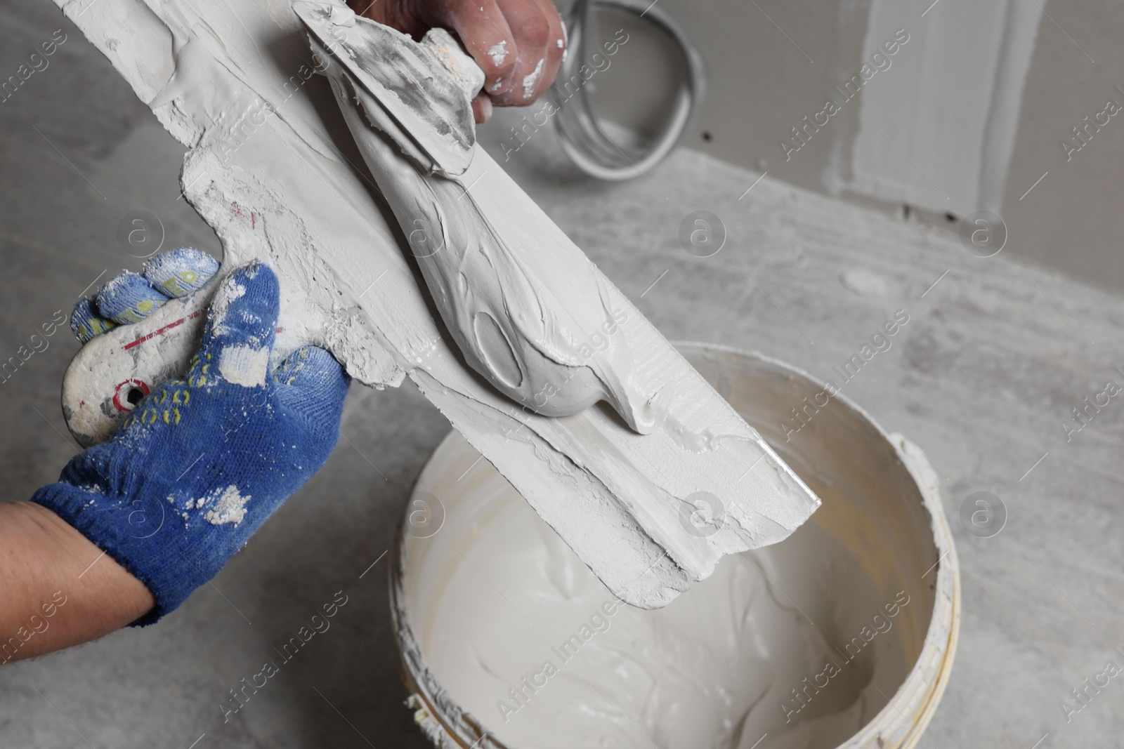 Photo of Professional worker putting plaster on putty knife indoors, closeup