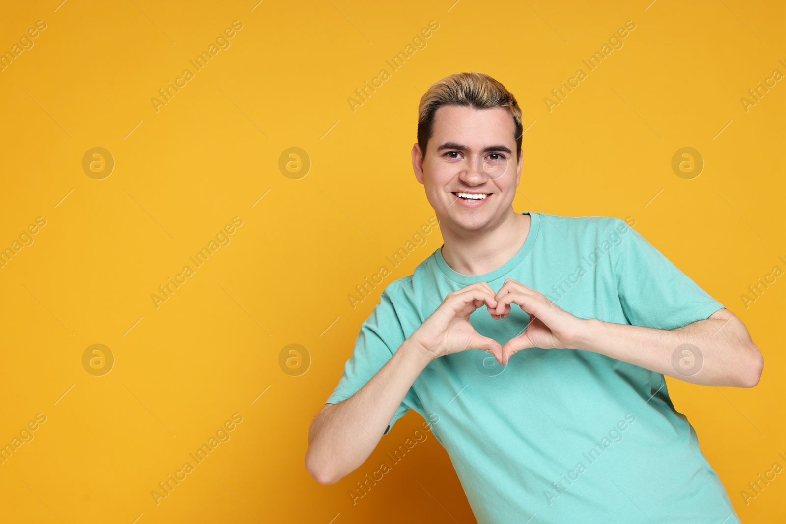 Photo of Young man showing heart gesture with hands on orange background, space for text