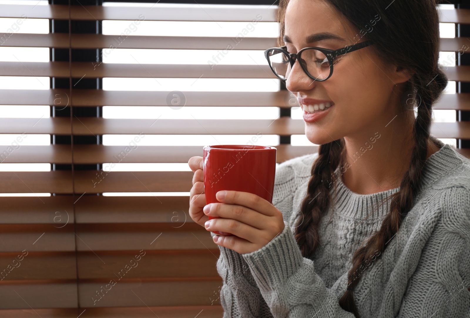 Image of Happy young woman with cup of hot drink near window. Lazy morning