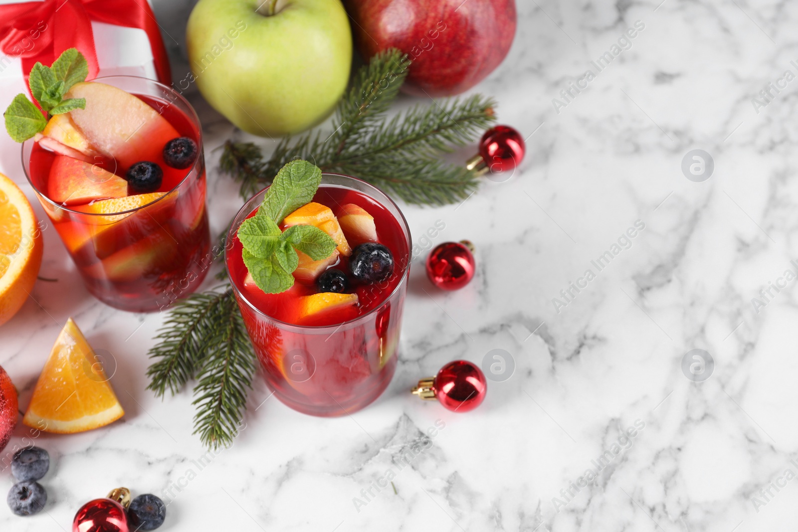 Photo of Aromatic Sangria drink in glasses, ingredients and Christmas decor on white marble table, space for text