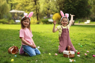 Photo of Easter celebration. Cute little girls in bunny ears hunting eggs outdoors