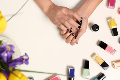 Photo of Woman applying nail polish near bottles on white table with flowers, top view