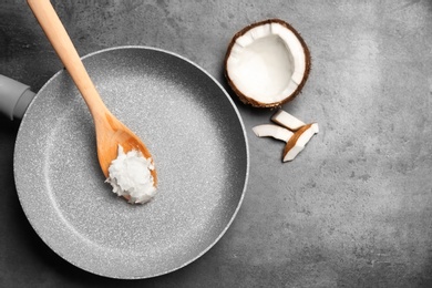 Photo of Frying pan with coconut oil and nut pieces on grey background