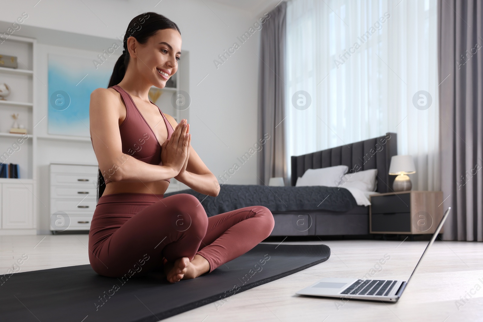 Photo of Beautiful young woman practicing Padmasana while watching online class on yoga mat at home, low angle view. Lotus pose